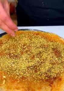 Garnishing the top of a Legendary Knafeh with bright green crushed pistachios.